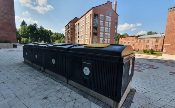 Syväkeräyssäiliörivi, jonka taustalla kerrostaloja, metsää ja vanha korkea tiilipiippu.