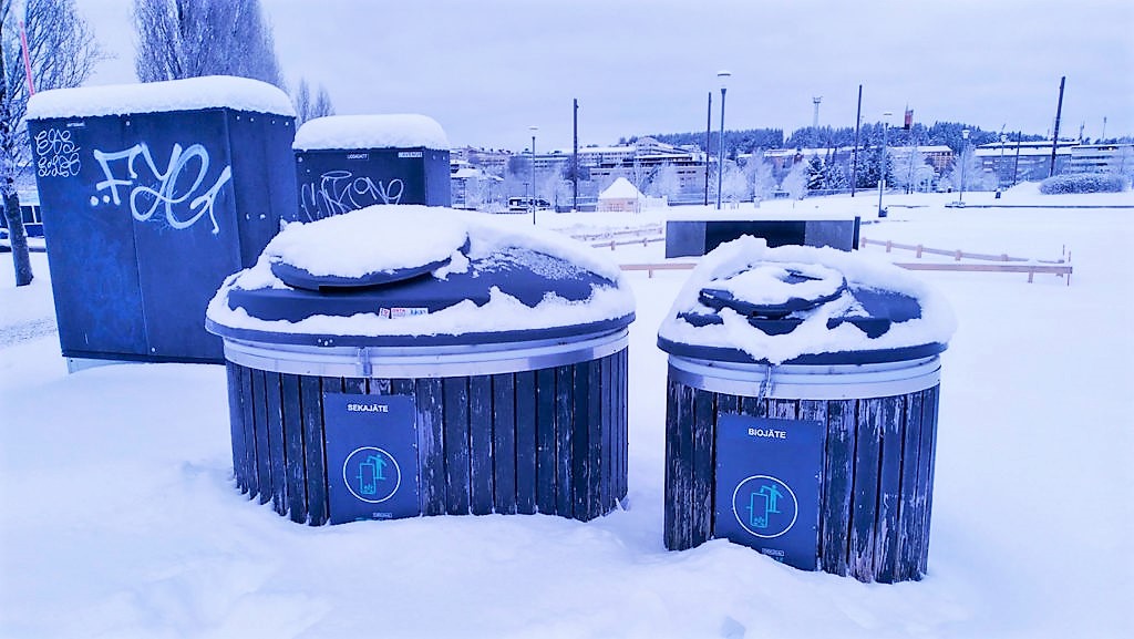Kuvassa kaksi suurta pyöreää lumen peittämää jätekeräysastiaa - vasemmalla suurempi sekajäteastia ja oikealla pienempi biojäteastia
