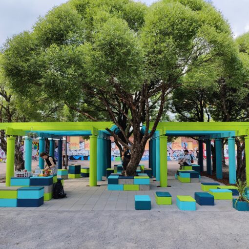 Kuvassa vehreiden puiden alla näkyvät värikkäät sinivihreät pergolat sekä istutuslaatikoita