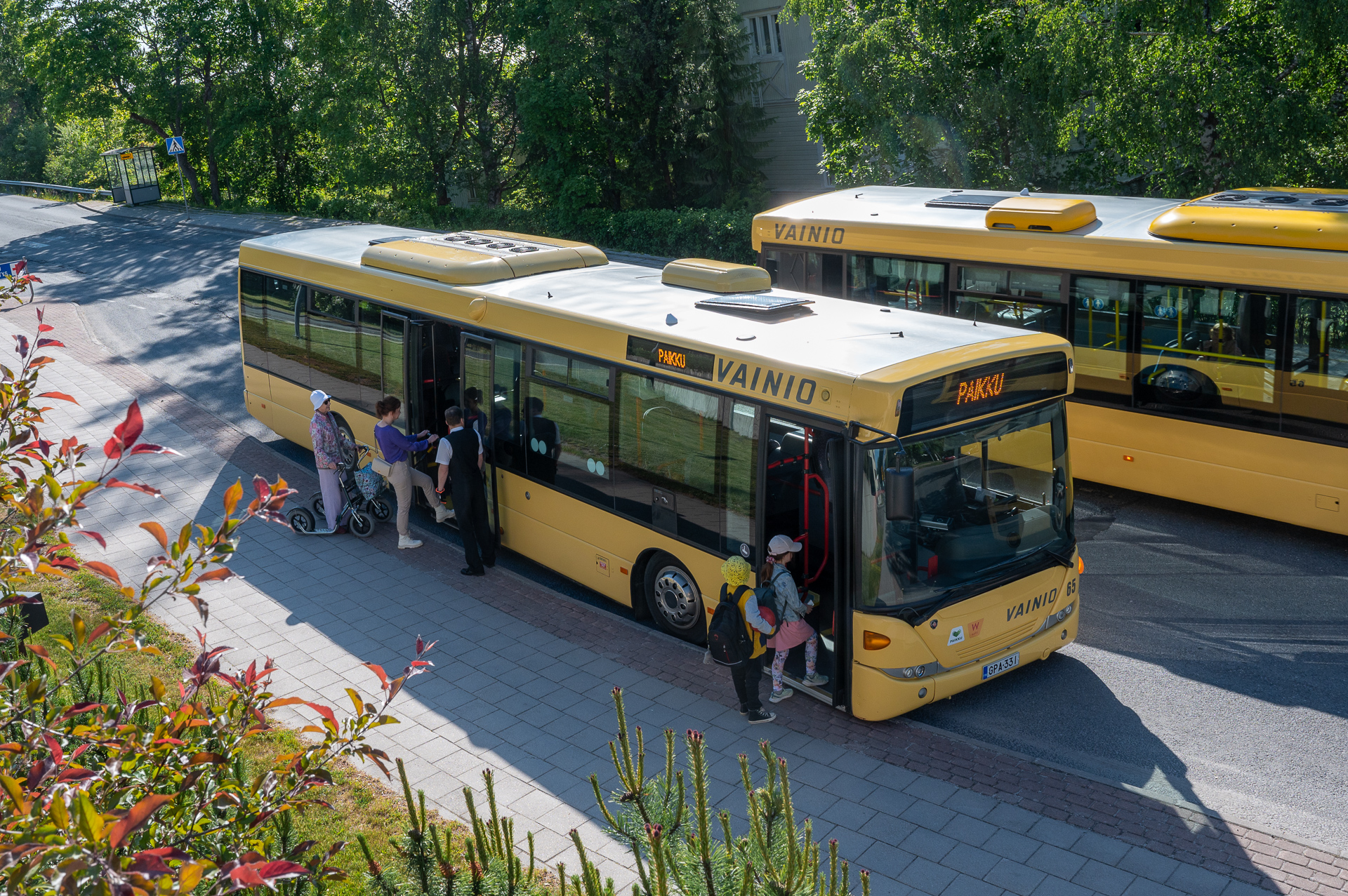 Kaksi keltaista bussia seisoo pysäkillä. Etummaiseen bussiin on nousemassa matkustajia etu- ja takaovista.