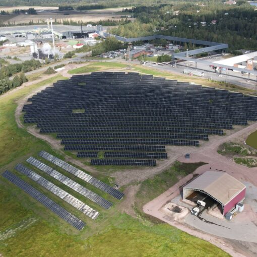 Bolidenin 3,9 MW aurinkovoimala Harjavallassa, ilmakuva. Paneelit ovat asennettuna kahden päällekkäisen ja kymmenien peräkkäisten paneelien muodostamissa riveissä, noin viiden metrin välein kattaen noin viiden hehtaarin alueen. Vieressä latorakennus, ympärillä nurmea. Taustalla näkyy teollisuusaluetta.