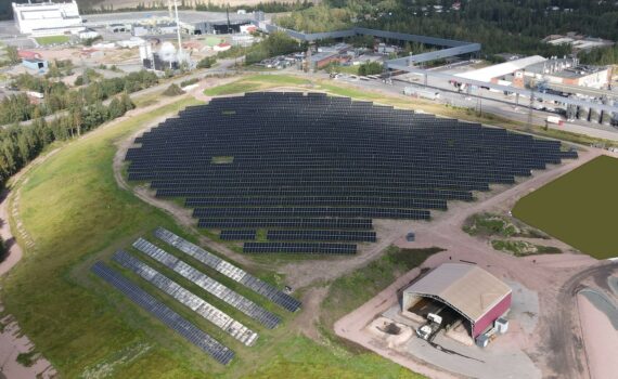Bolidenin 3,9 MW aurinkovoimala Harjavallassa, ilmakuva. Paneelit ovat asennettuna kahden päällekkäisen ja kymmenien peräkkäisten paneelien muodostamissa riveissä, noin viiden metrin välein kattaen noin viiden hehtaarin alueen. Vieressä latorakennus, ympärillä nurmea. Taustalla näkyy teollisuusaluetta.