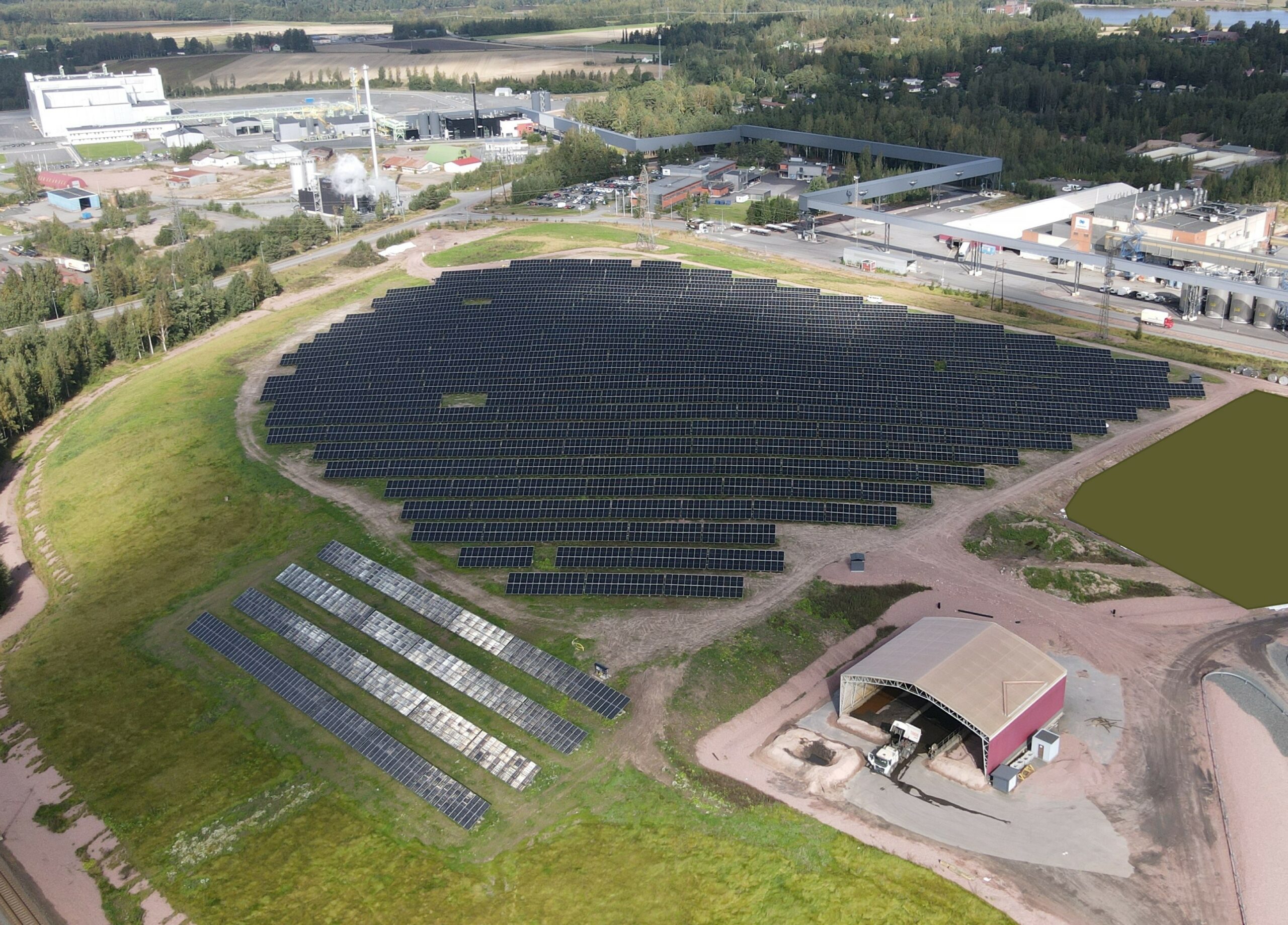 Bolidenin 3,9 MW aurinkovoimala Harjavallassa, ilmakuva. Paneelit ovat asennettuna kahden päällekkäisen ja kymmenien peräkkäisten paneelien muodostamissa riveissä, noin viiden metrin välein kattaen noin viiden hehtaarin alueen. Vieressä latorakennus, ympärillä nurmea. Taustalla näkyy teollisuusaluetta.