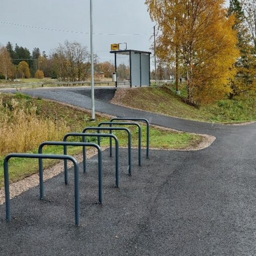 Pöyräpysäköintipaikka linja-autoasemalla. Metalliset kaaret etualalla. Taustalla linja-autopysäkki. Harmaa taivas, taustalla puita, joiden lehdet ovat kellastuneet.
