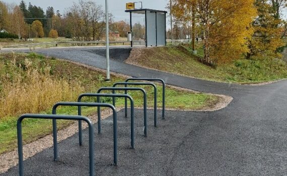Pöyräpysäköintipaikka linja-autoasemalla. Metalliset kaaret etualalla. Taustalla linja-autopysäkki. Harmaa taivas, taustalla puita, joiden lehdet ovat kellastuneet.