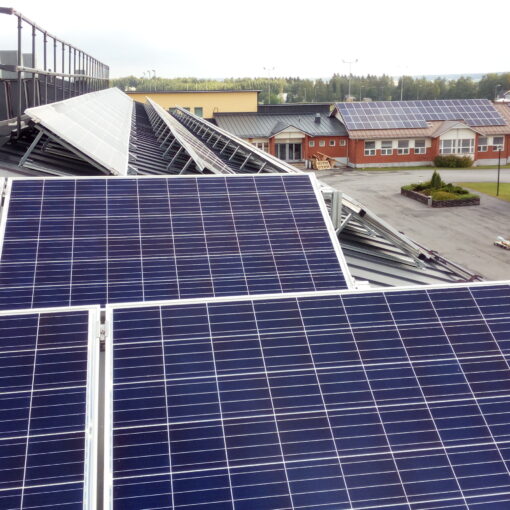 Aurinkopaneeleja, taustalla punainen rakennus ja peltomaisema.