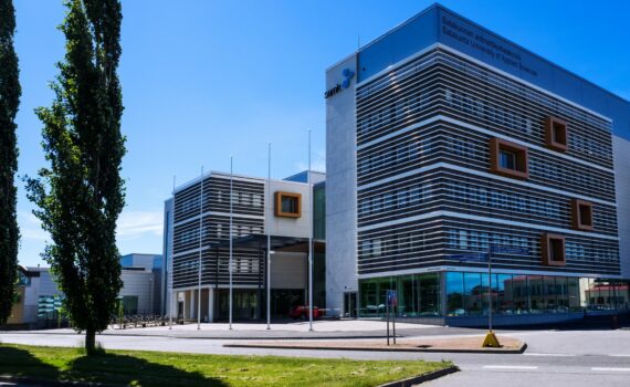 SAMKin Porin kampus. Kulmikas moderni rakennus. Etualalla asfalttia, nurmikaistale ja kaksi havupuuta. Taivas on sininen ja kirkas.