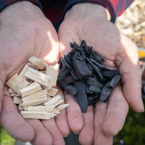 Kädet, joissa toisessa kourassa pientä puusilppua ja toisessa biohiiltä.