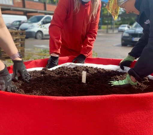 Lapsia istutussäkin ympärillä hansikoidut kädet mullassa.