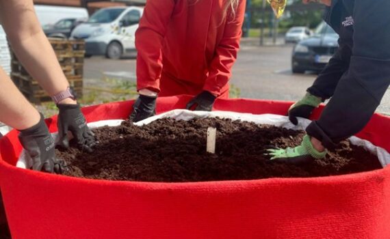 Lapsia istutussäkin ympärillä hansikoidut kädet mullassa.