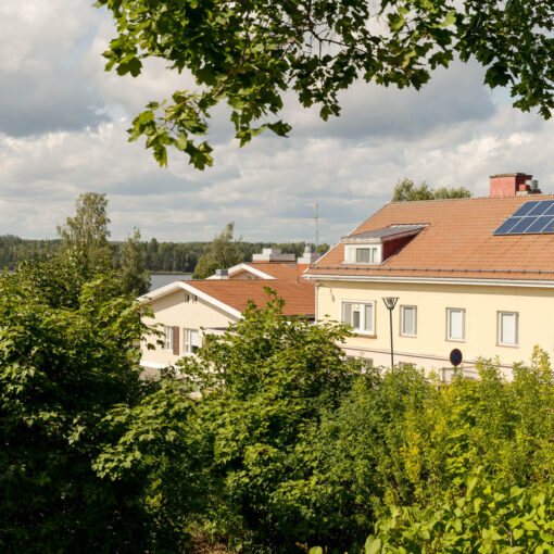 Puiden välistä pilkottaa keltainen kivirakennus, jonka katolla on aurinkopaneeleja.