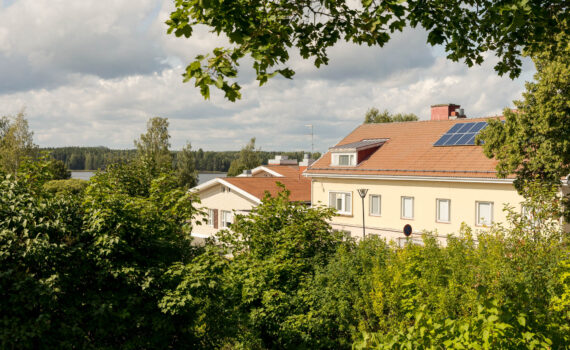 Puiden välistä pilkottaa keltainen kivirakennus, jonka katolla on aurinkopaneeleja.