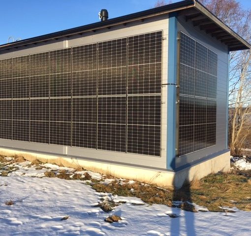 Nikus vedenottamon aurinkojärjestelmä. Kuution mallinen rakennus, jonka näkyvillä sivuilla on aurinkopaneeleja. Maassa on ohut kerros lunta.